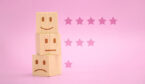 Wooden blocks showing sad to happy faces stacked with star rating on pink background,
