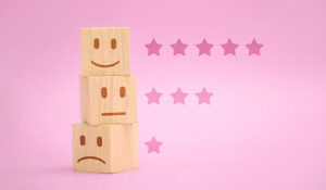 Wooden blocks showing sad to happy faces stacked with star rating on pink background,