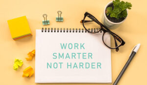Work smarter, not harder Text written on notepad page, glasses, pen, stationery on yellow background.
