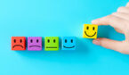 Hand selecting smiling face block from row of colorful emotion icons representing customer satisfaction