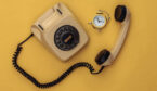 Old fashioned telephone with a clock on a yellow background