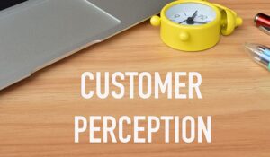 The word customer perception written on a wooden table with a laptop and mini clock in the background
