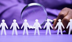 Row of paper people with a human hand holding a magnifying glass