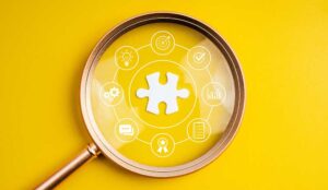 Magnifying glass focusing on puzzle piece with business strategy icons, representing elements of employee experience
